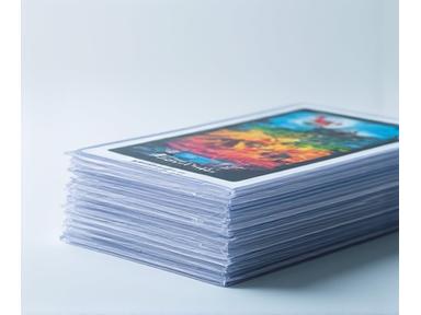 Stack of colorful, transparent premium card sleeves next to a deck of board game cards.